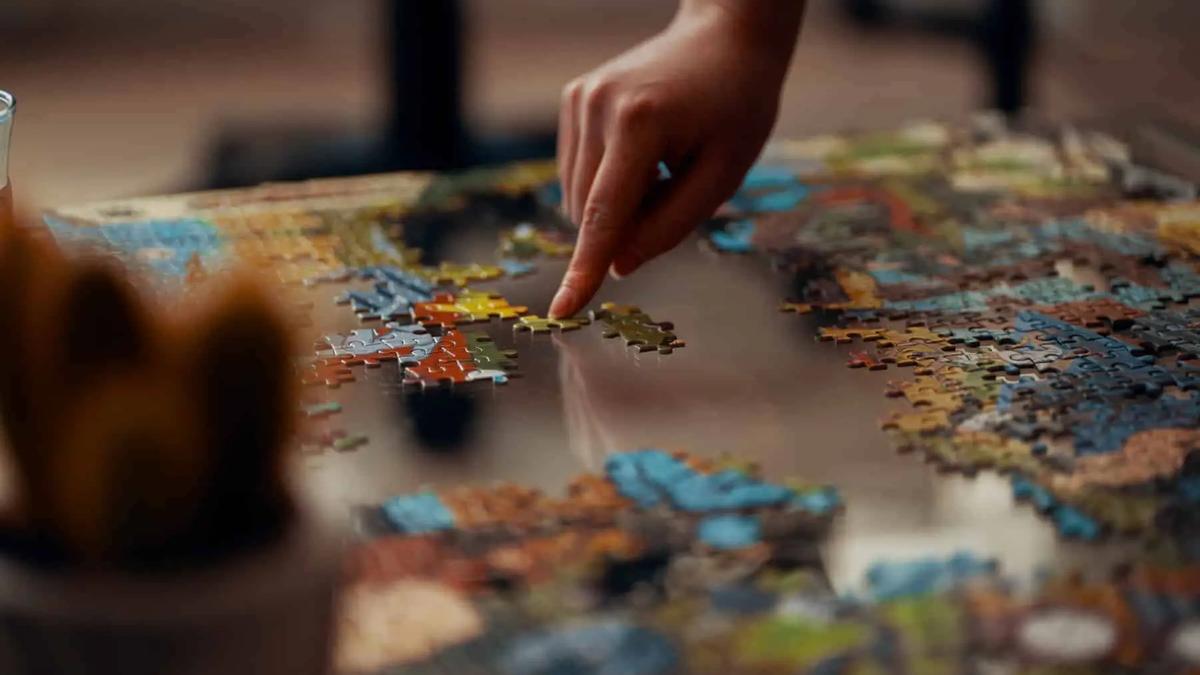A hand placing a piece into a partly finished jigsaw puzzle on a table