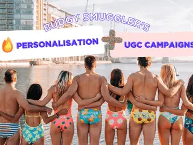 People in colourful swimwear standing arm in arm by a waterfront, with a Budgy Smuggler campaign banner overlay.