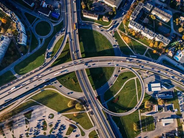 Vista aerea de un cruce de autopistas con rampas curvas rodeado de zonas verdes y edificios