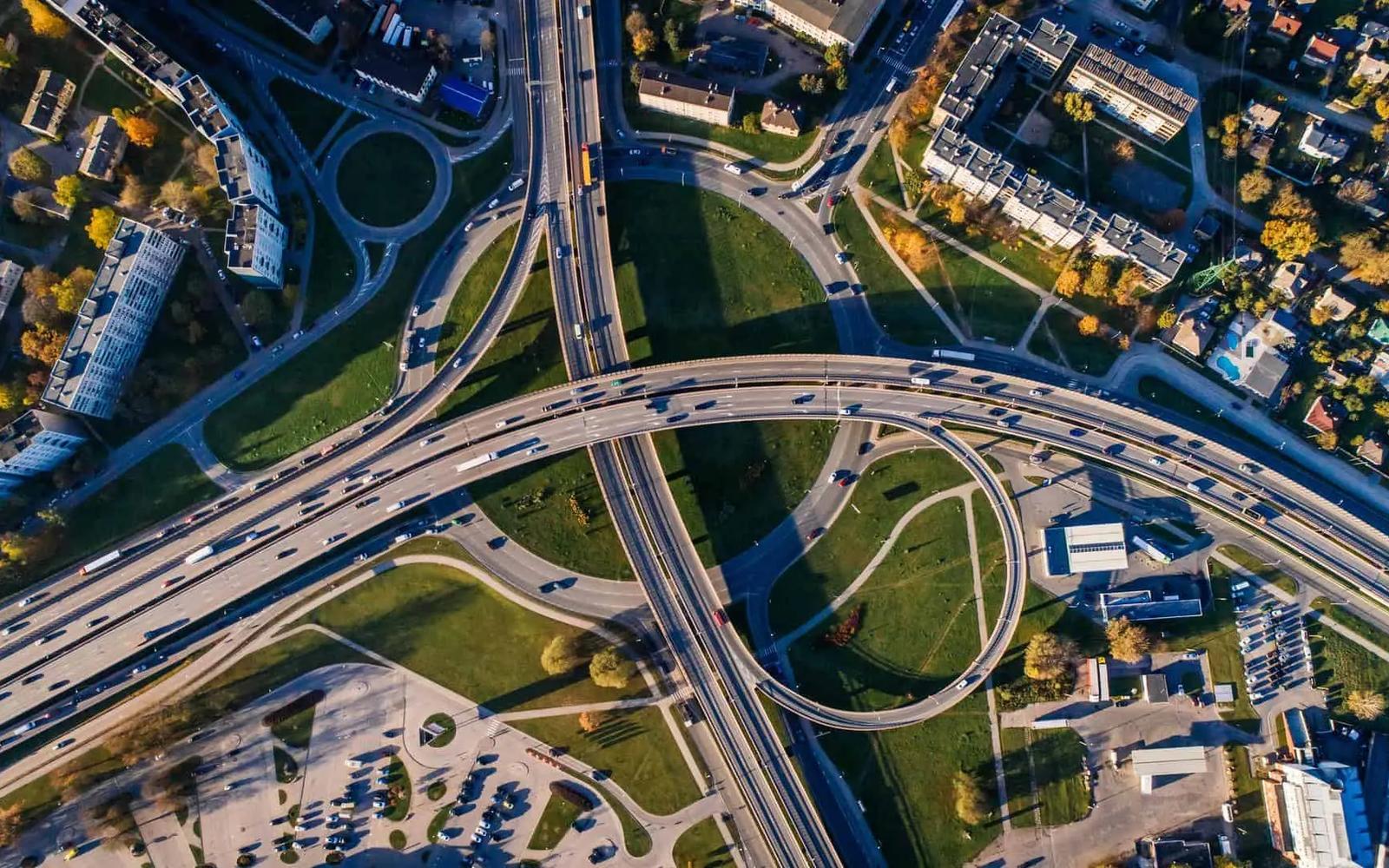 Aerial view of a multi-lane highway interchange with looping ramps surrounded by green space and buildings