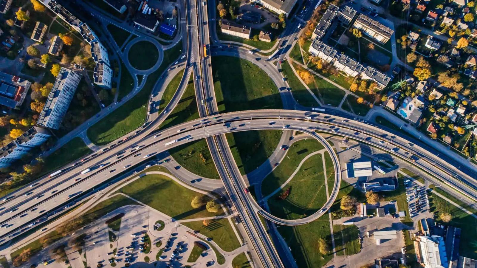 Vista aerea de un cruce de autopistas con rampas curvas rodeado de zonas verdes y edificios