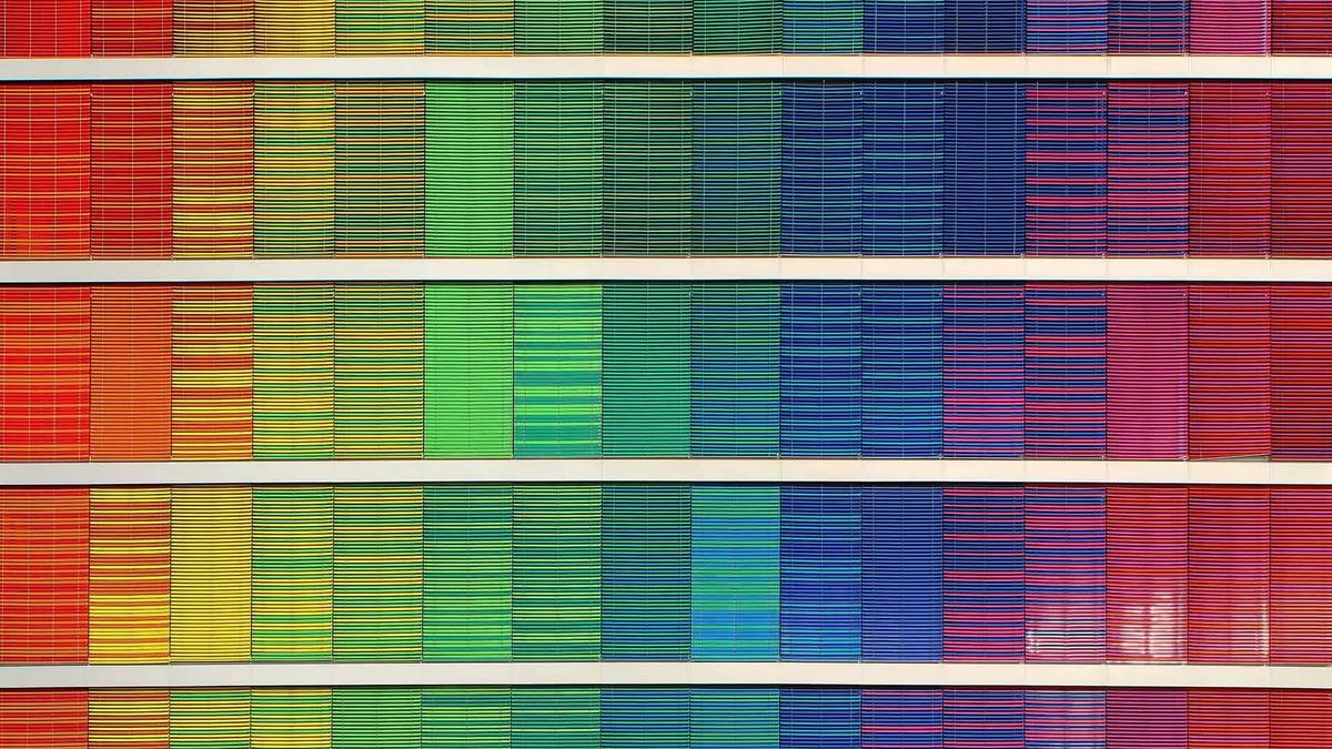 Rows of colourful window blinds forming a rainbow gradient pattern on a building facade