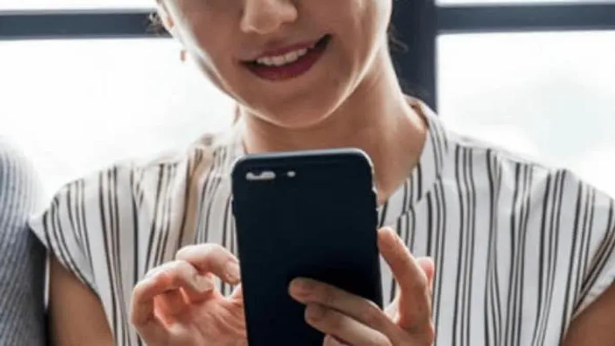 A smiling woman in a striped top holding and looking at a smartphone, seated between others