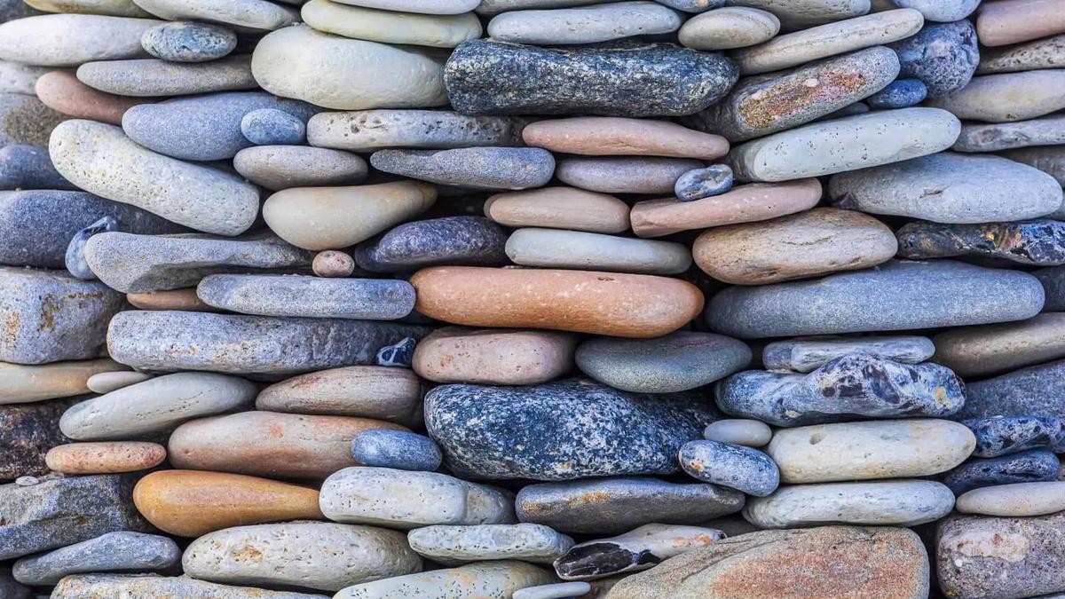 Stacked, smooth, flat, grey, blue, and brown river stones form a wall, filling the frame