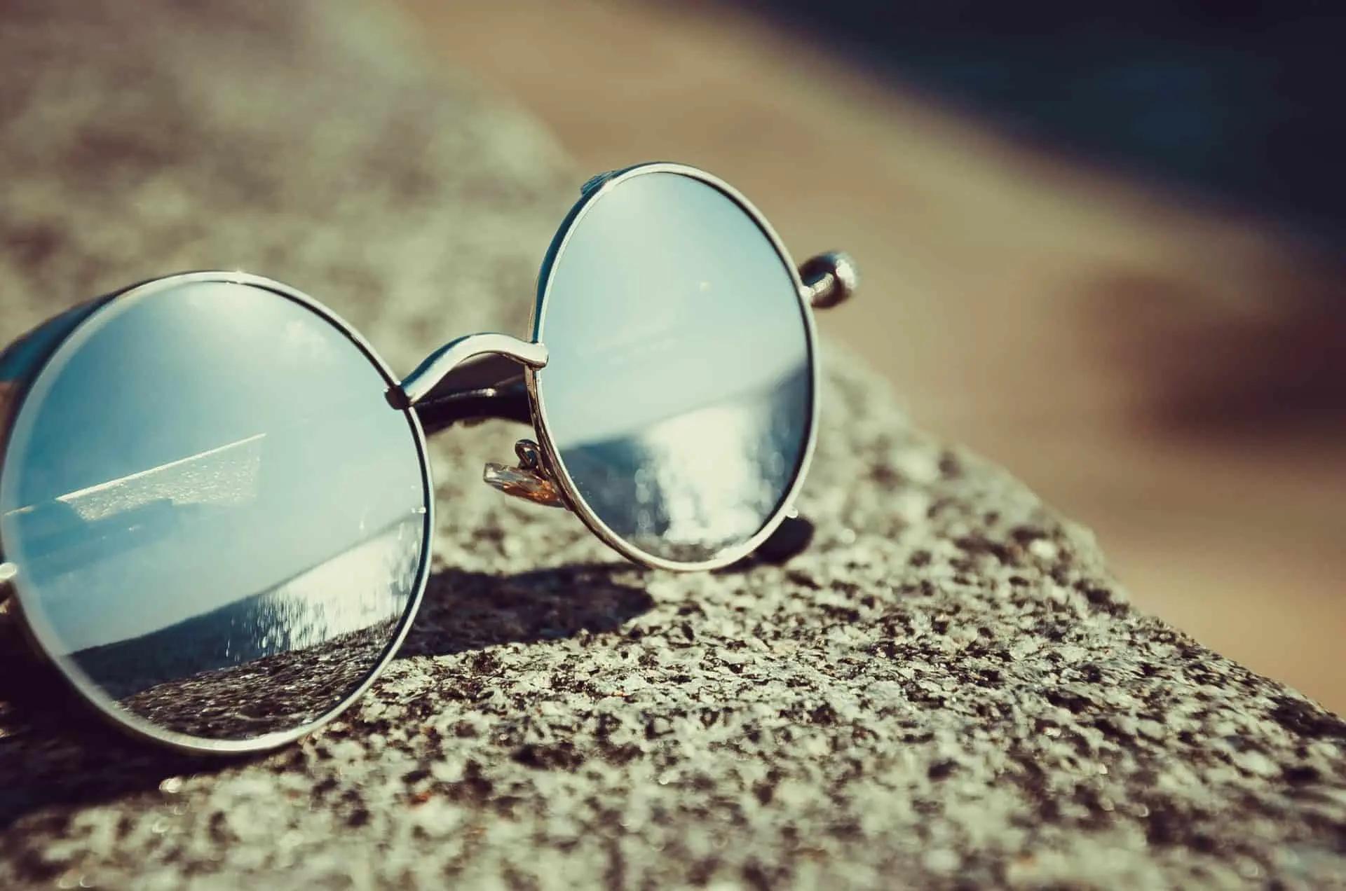 Round mirrored sunglasses resting on a textured stone surface in sunlight