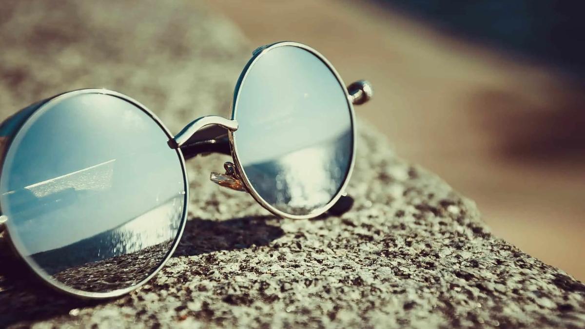 Round mirrored sunglasses resting on a textured stone surface in sunlight
