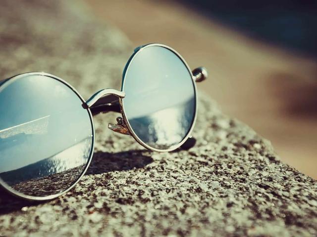 Gafas de sol redondas con lentes espejadas apoyadas sobre una piedra al sol