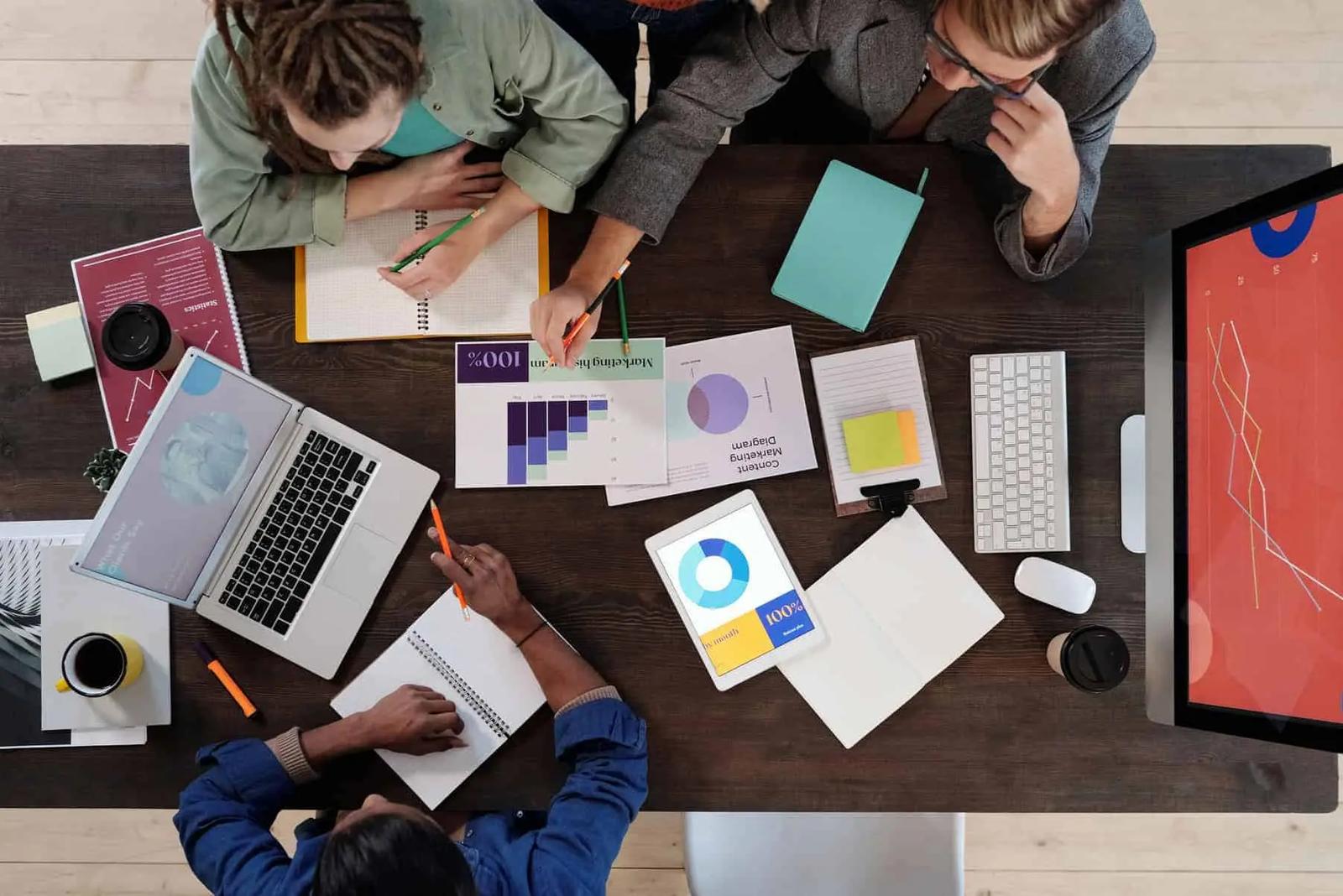 Overhead view of a team at a desk reviewing marketing charts, laptops and a tablet with graphs