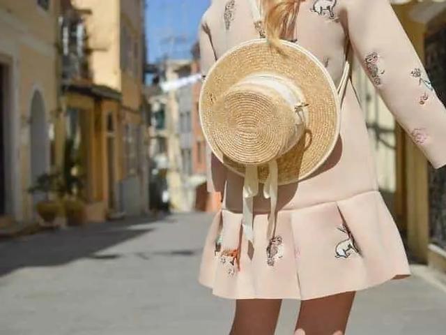 Mujer con un vestido rosa estampado que lleva un sombrero de paja, caminando por una calle estrecha
