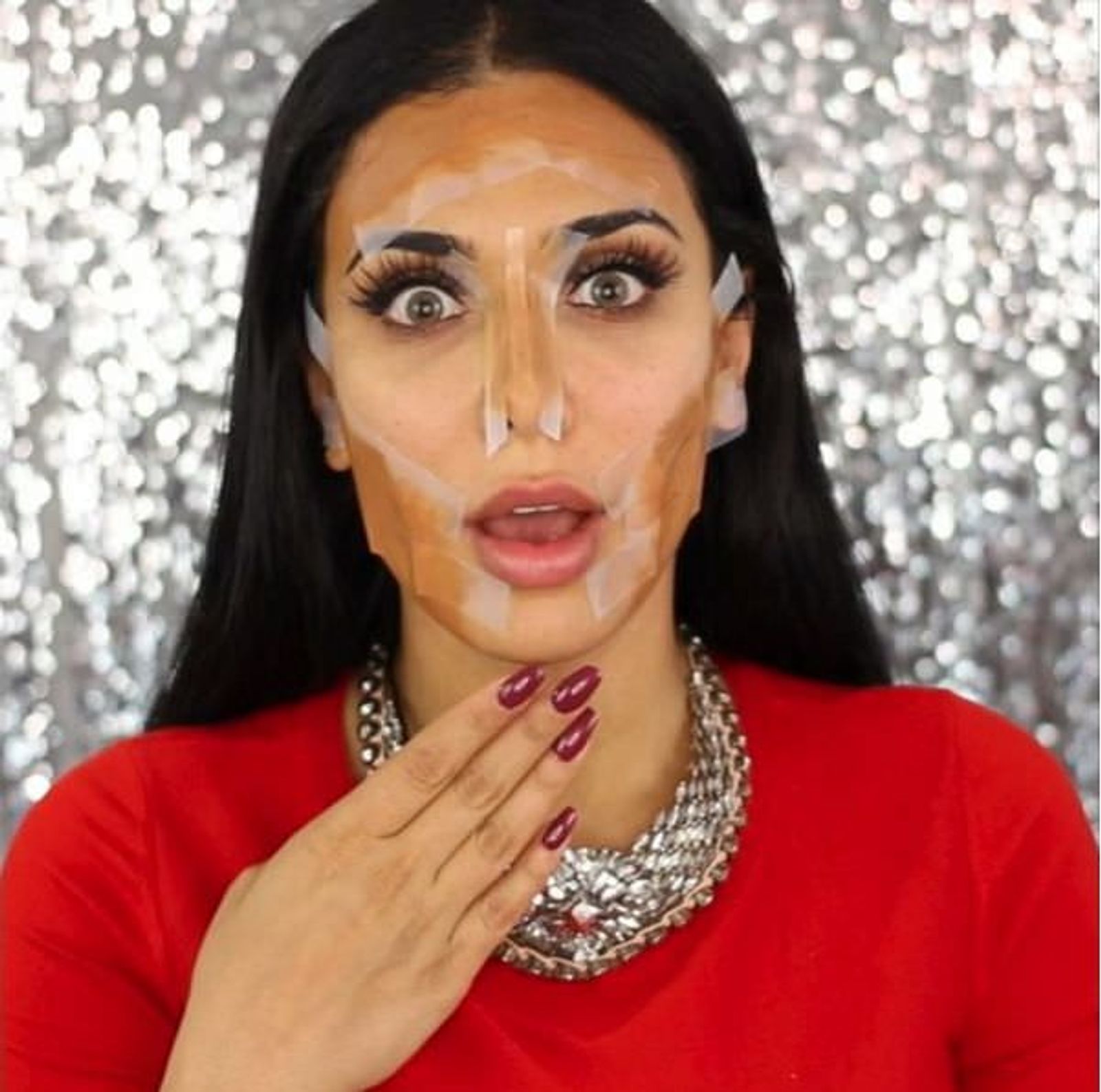 Una mujer con líneas de contouring marcadas en el rostro, con top rojo y collar grueso plateado.