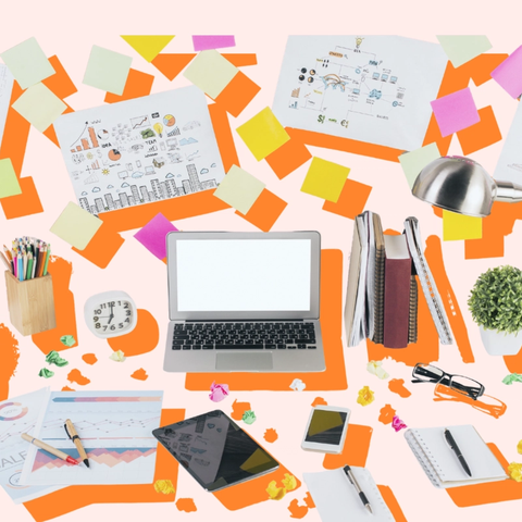 Escritorio desordenado con laptop, tablet, teléfono, papeles, bolígrafos, notas adhesivas, papel arrugado y una lámpara. Fondo rosa claro y naranja.