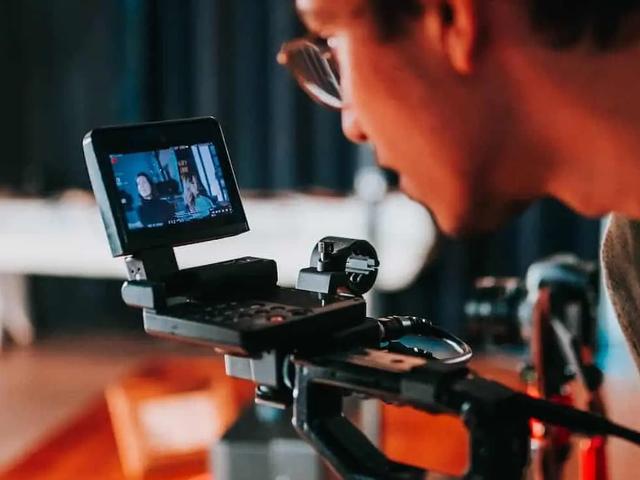 Una persona con gafas observa de cerca la pantalla de un monitor de cámara mientras filma