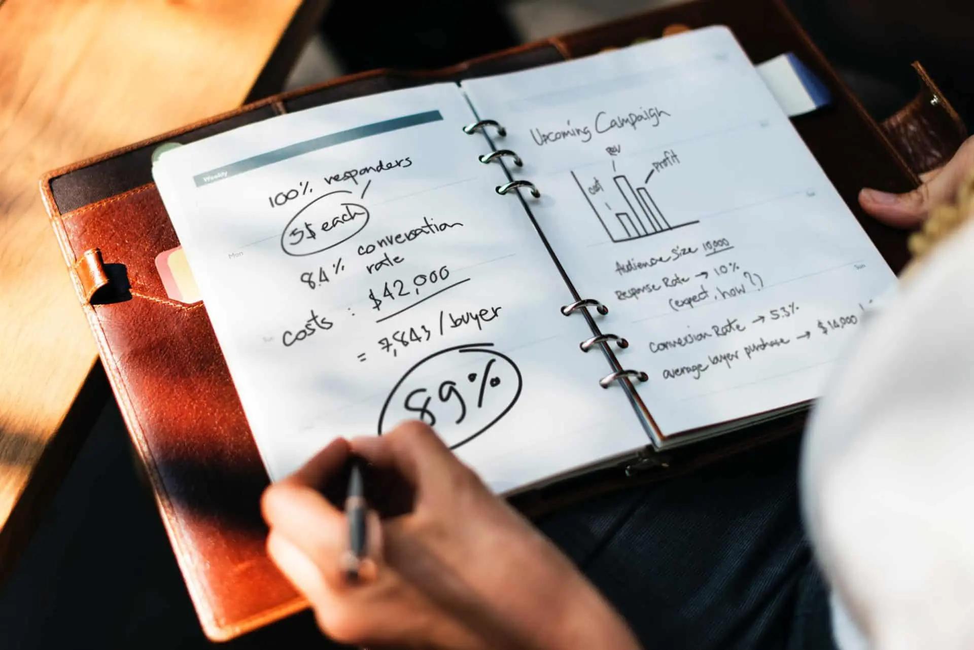 A hand writing campaign numbers and a bar chart in a leather-bound planner