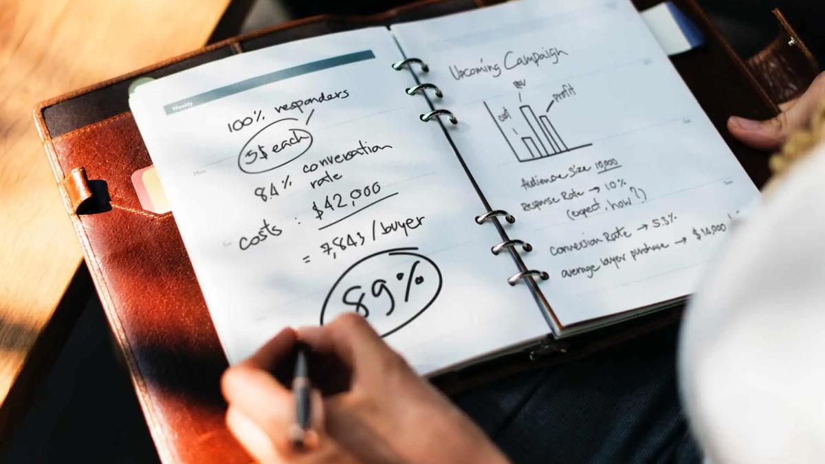 A hand writing campaign numbers and a bar chart in a leather-bound planner