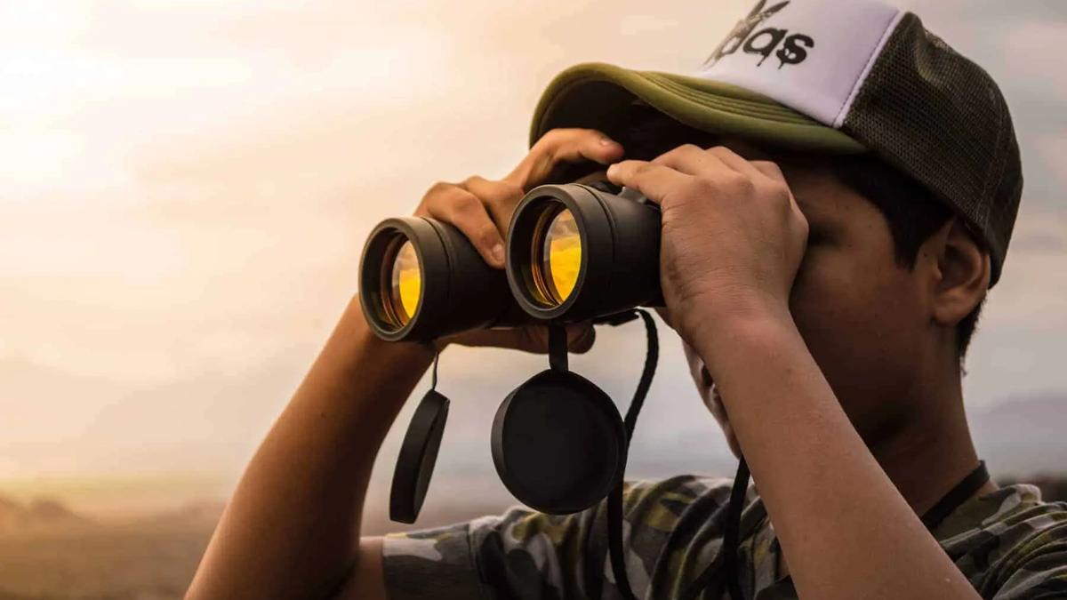 Persona con gorra mirando a través de binoculares hacia un paisaje neblinoso