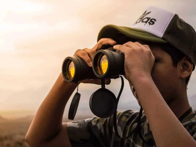 Persona con gorra mirando a través de binoculares hacia un paisaje neblinoso