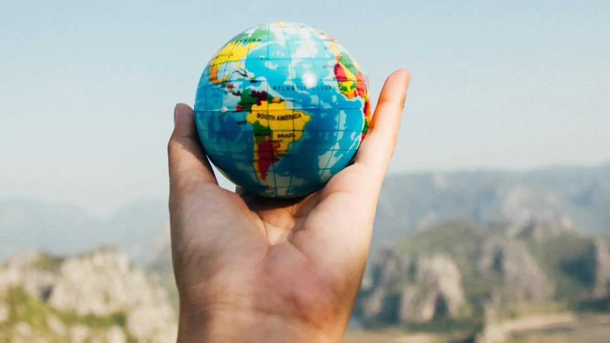 A hand holding a small toy globe against a mountain landscape