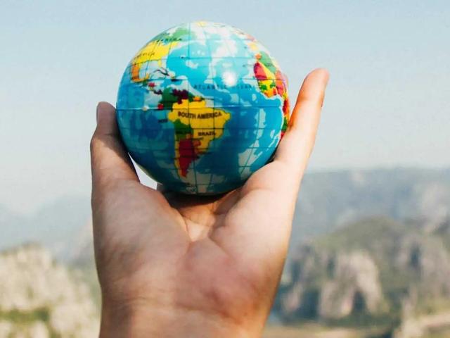 Una mano sostiene un pequeño globo terráqueo de juguete frente a un paisaje montañoso