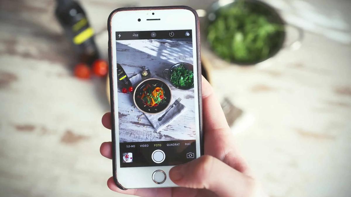 Hand holding a phone photographing a plated salad on a wooden table