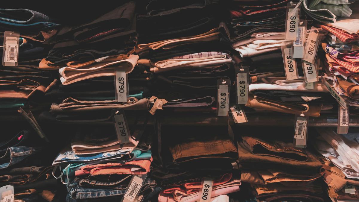 Prendas de ropa dobladas y apiladas en estantes con etiquetas de papel sujetas