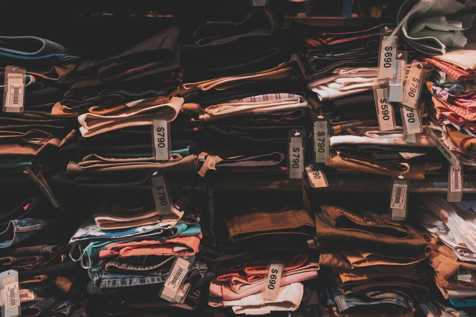Folded clothing stacked on shelves with paper tags clipped to each pile