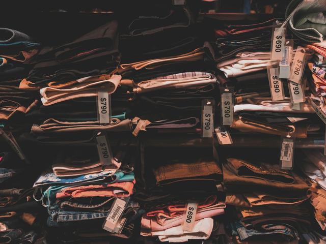 Prendas de ropa dobladas y apiladas en estantes con etiquetas de papel sujetas