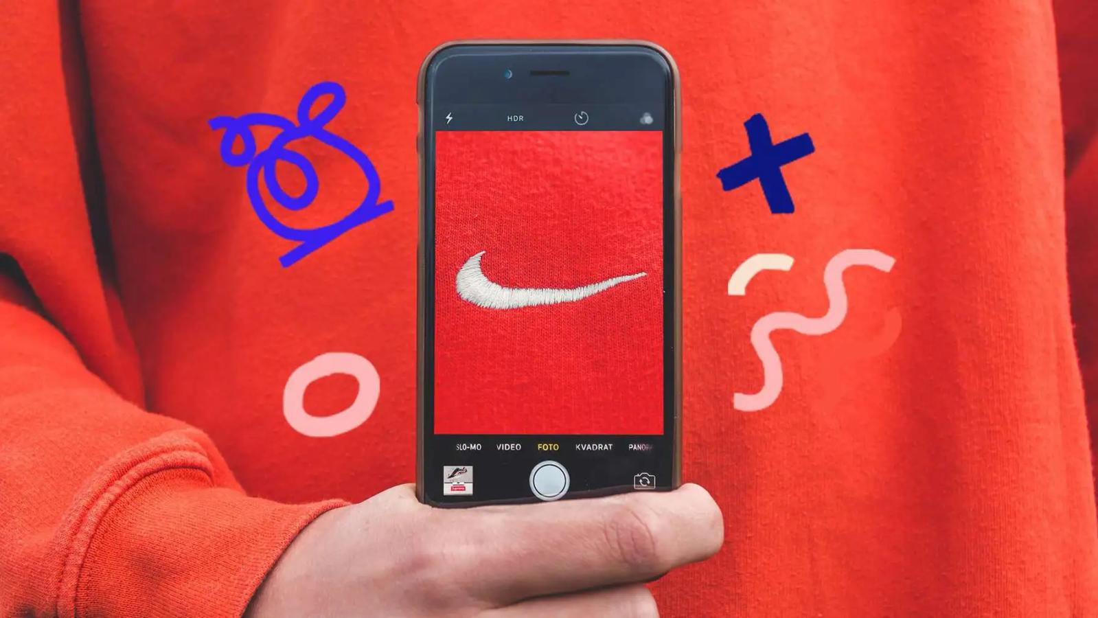 Una mano sostiene un telefono fotografiando el logo de Nike en una sudadera naranja, con garabatos alrededor
