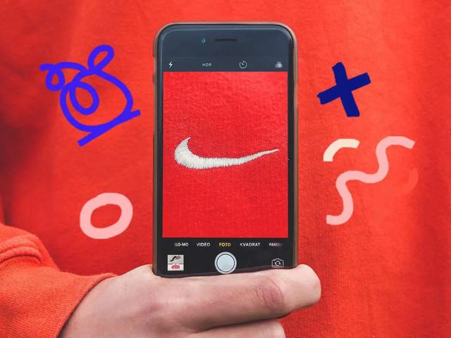 Una mano sostiene un telefono fotografiando el logo de Nike en una sudadera naranja, con garabatos alrededor
