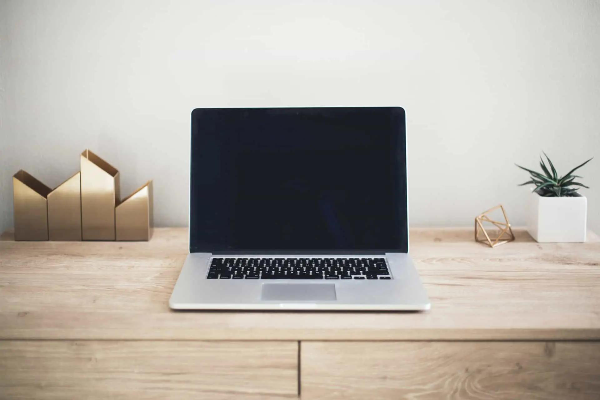 A laptop with a blank dark screen on a wooden desk with decor and a small plant
