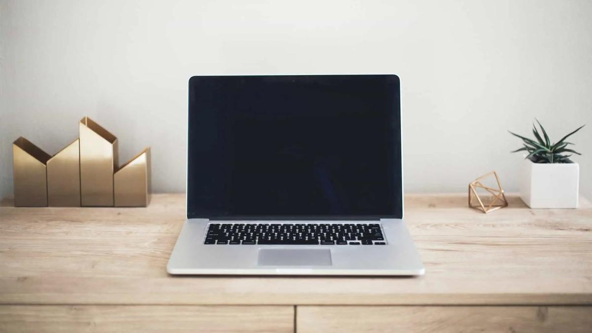 A laptop with a blank dark screen on a wooden desk with decor and a small plant