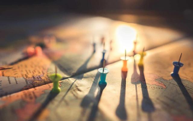 Colorful pushpins stuck in a paper map, casting long shadows in warm light