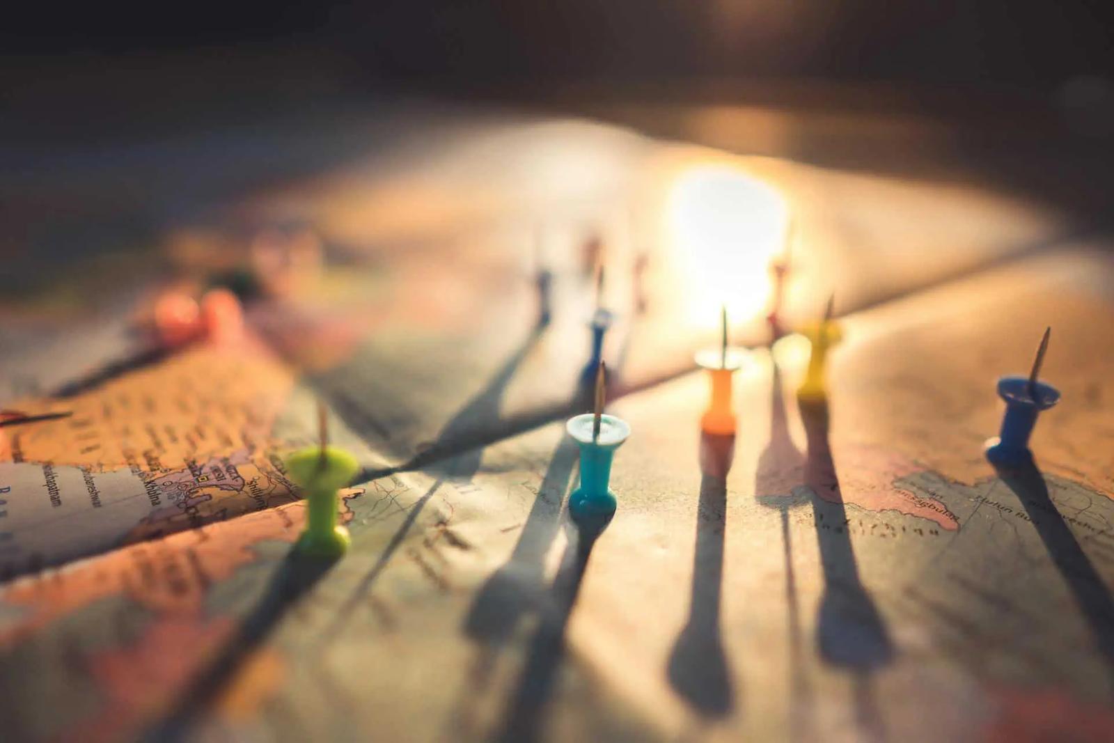 Colorful pushpins stuck in a paper map, casting long shadows in warm light