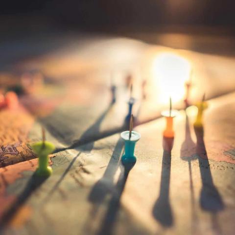 Colorful pushpins stuck in a paper map, casting long shadows in warm light