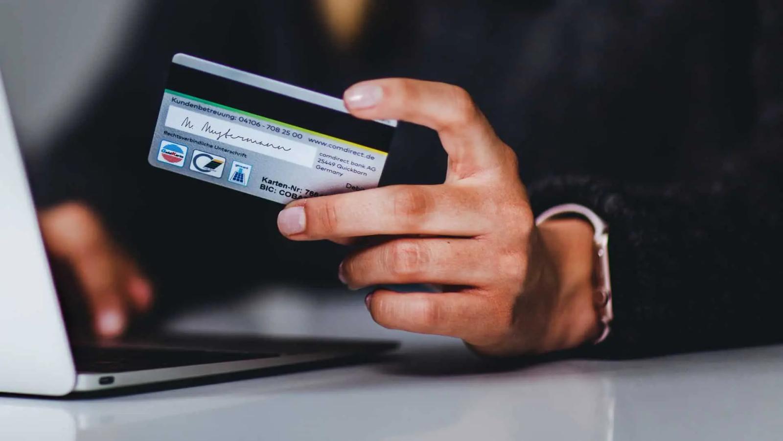 A hand holding a bank card while typing on a laptop keyboard