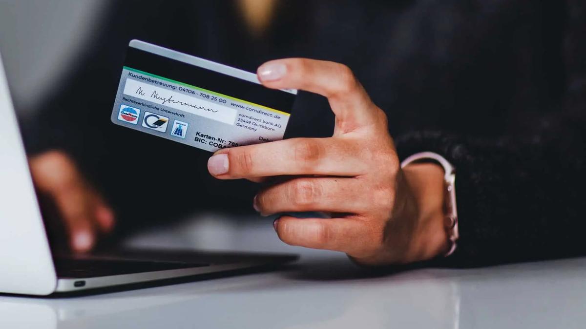 A hand holding a bank card while typing on a laptop keyboard