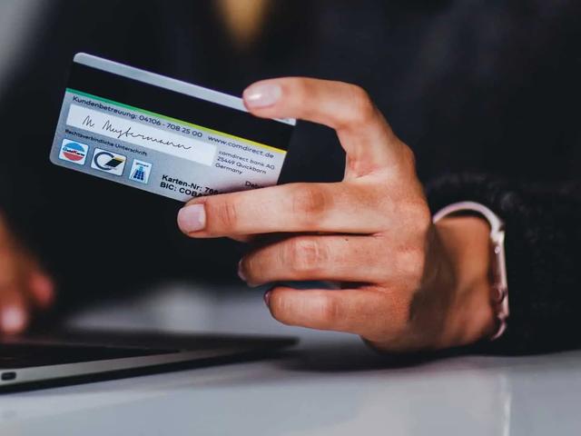 Una mano sostiene una tarjeta bancaria frente a un portátil
