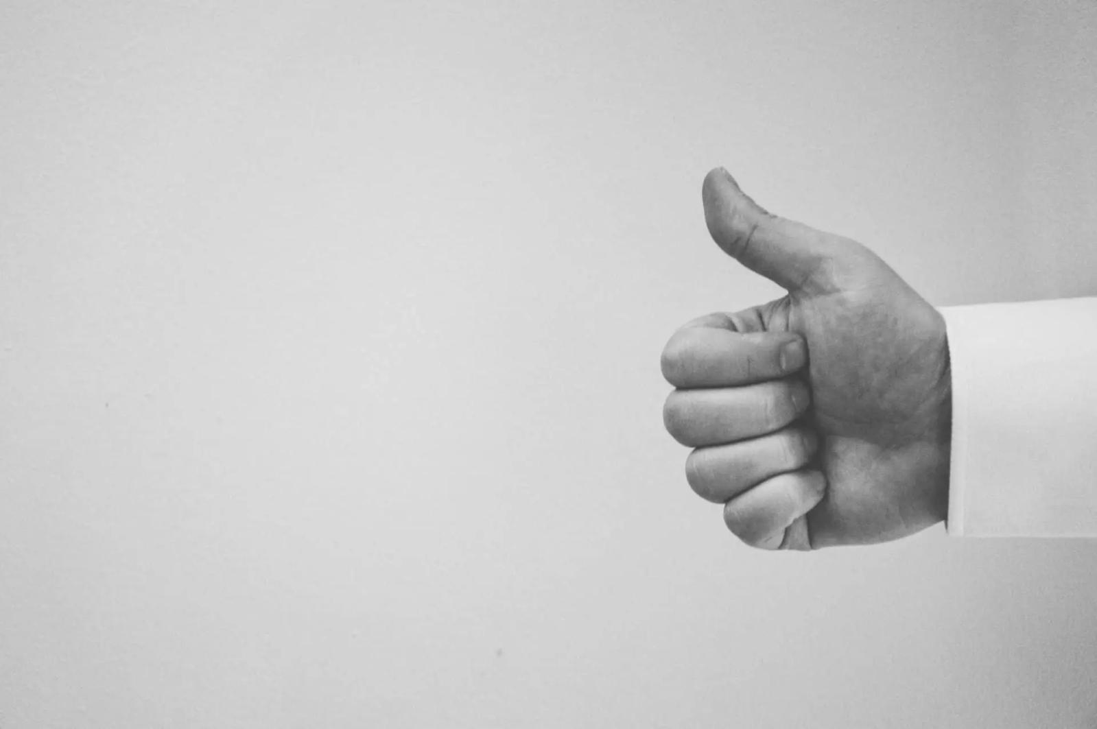 Fotografía en blanco y negro de una mano haciendo un gesto de pulgar hacia arriba sobre un fondo liso