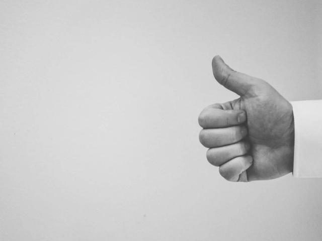 Black and white photo of a hand giving a thumbs up gesture against a plain background