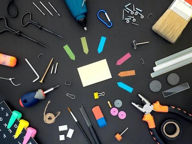Various tools and office supplies arranged on a black surface, including a screwdriver, pliers, glue gun, and sticky notes