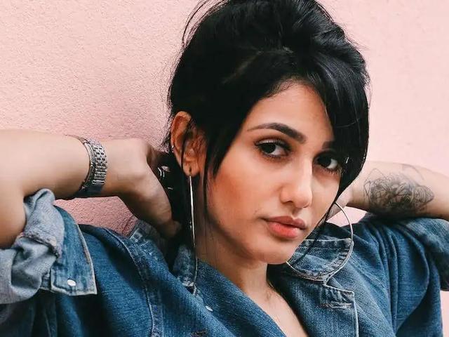 Mujer con chaqueta vaquera y aretes de aro posando frente a una pared rosa