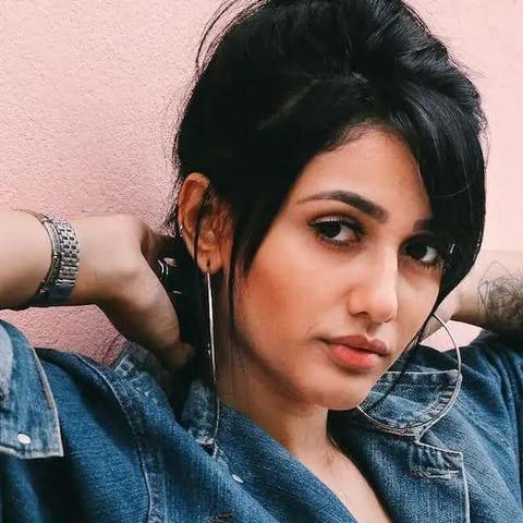 Woman in a denim jacket and hoop earrings posing against a pink wall