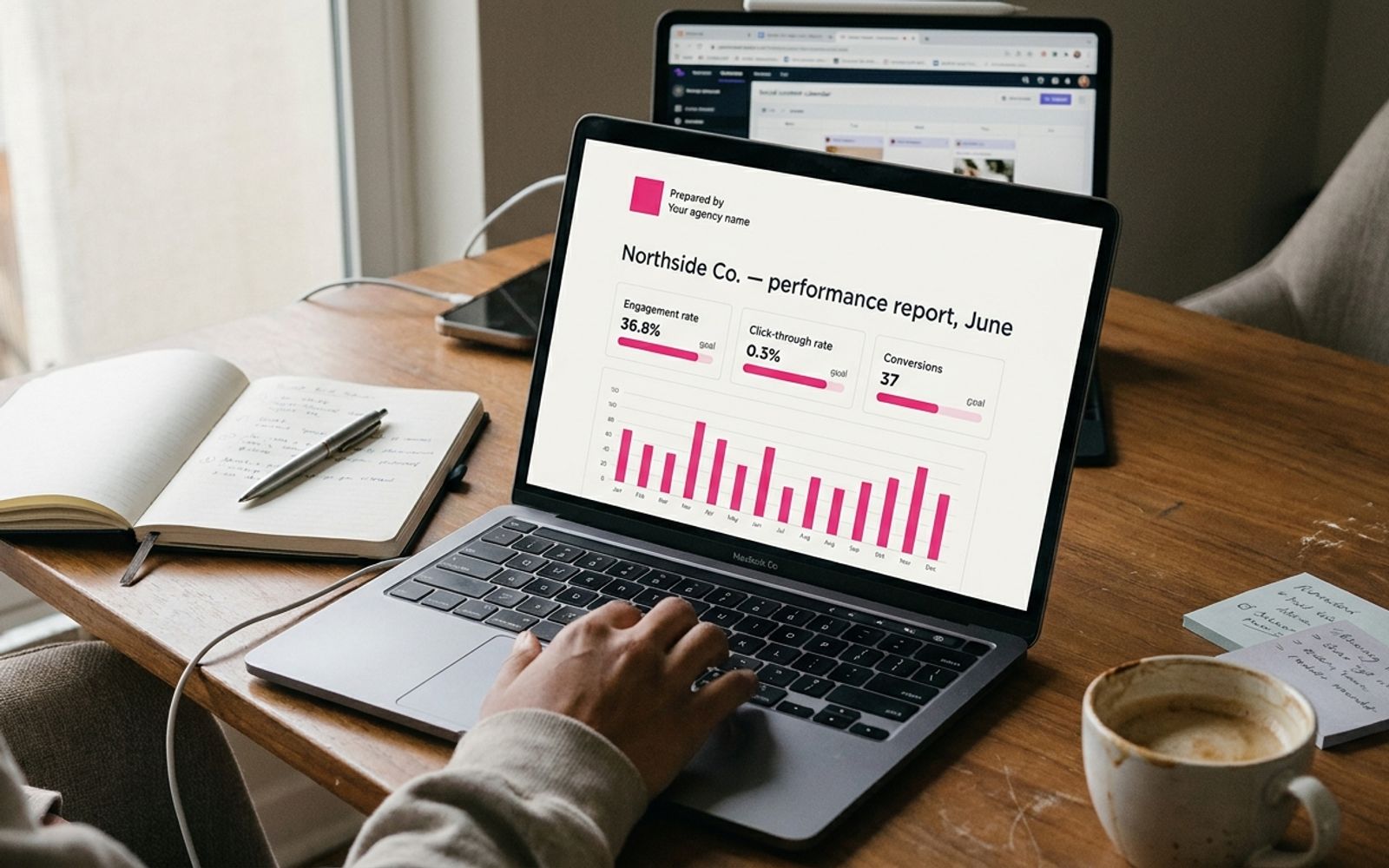 Laptop on a real desk showing a clean one-page client social media report with KPI tiles and a pink bar chart.