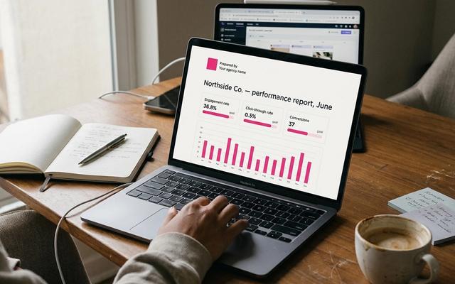 Laptop on a real desk showing a clean one-page client social media report with KPI tiles and a pink bar chart.