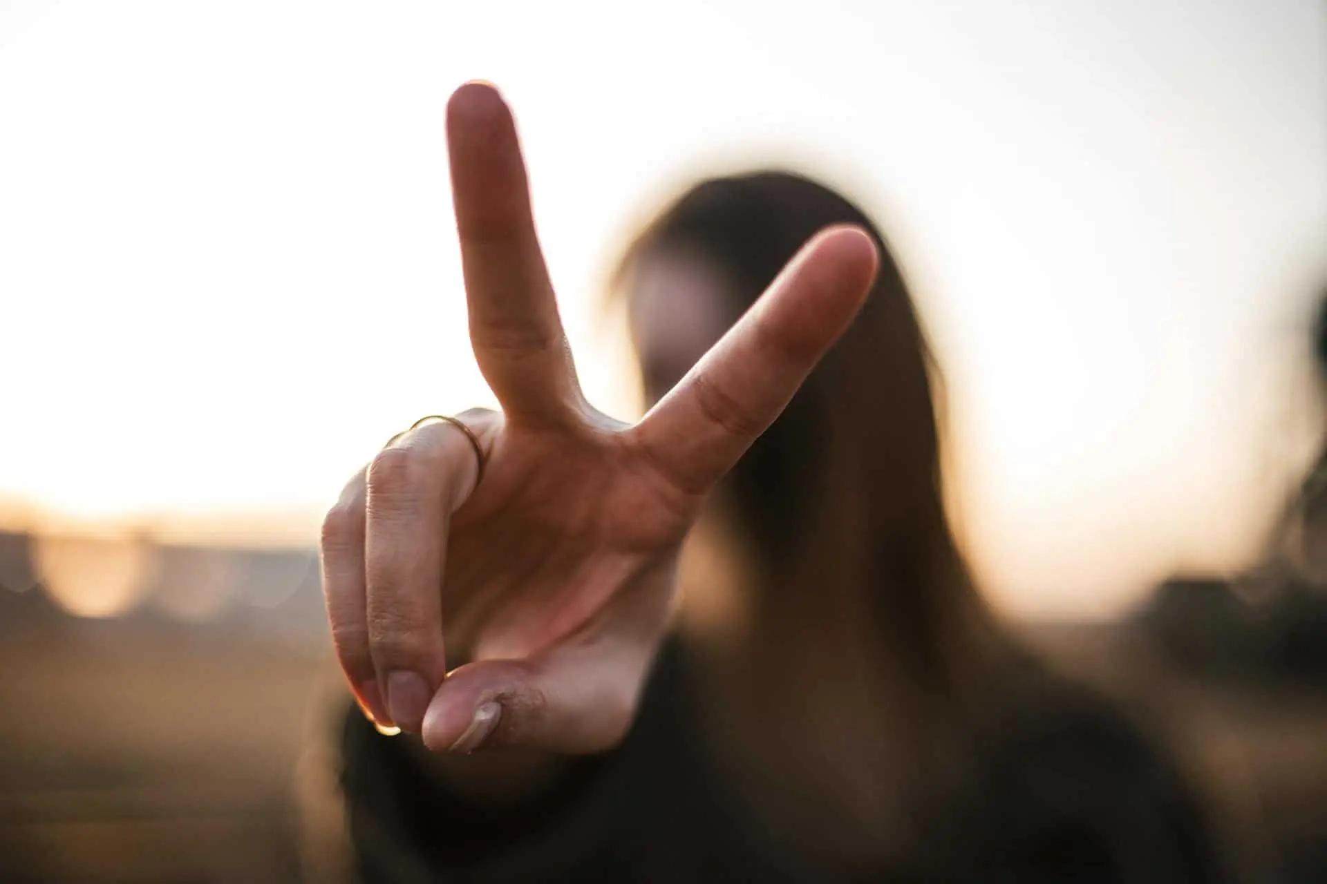 A woman holds up a peace sign toward the camera against a sunset backdrop