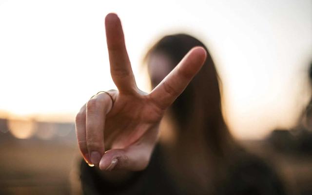 A woman holds up a peace sign toward the camera against a sunset backdrop