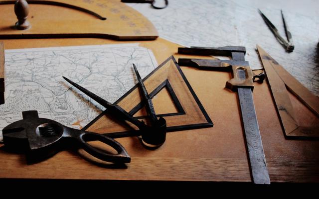 Old maps, compasses, a ruler and drafting tools laid out on a wooden desk