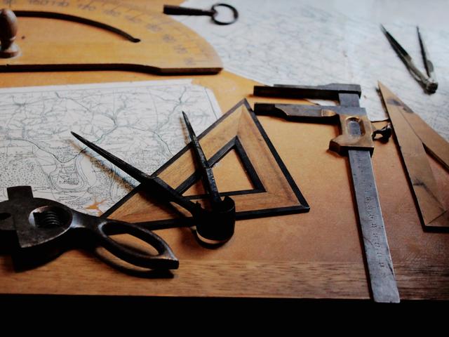 Old maps, compasses, a ruler and drafting tools laid out on a wooden desk