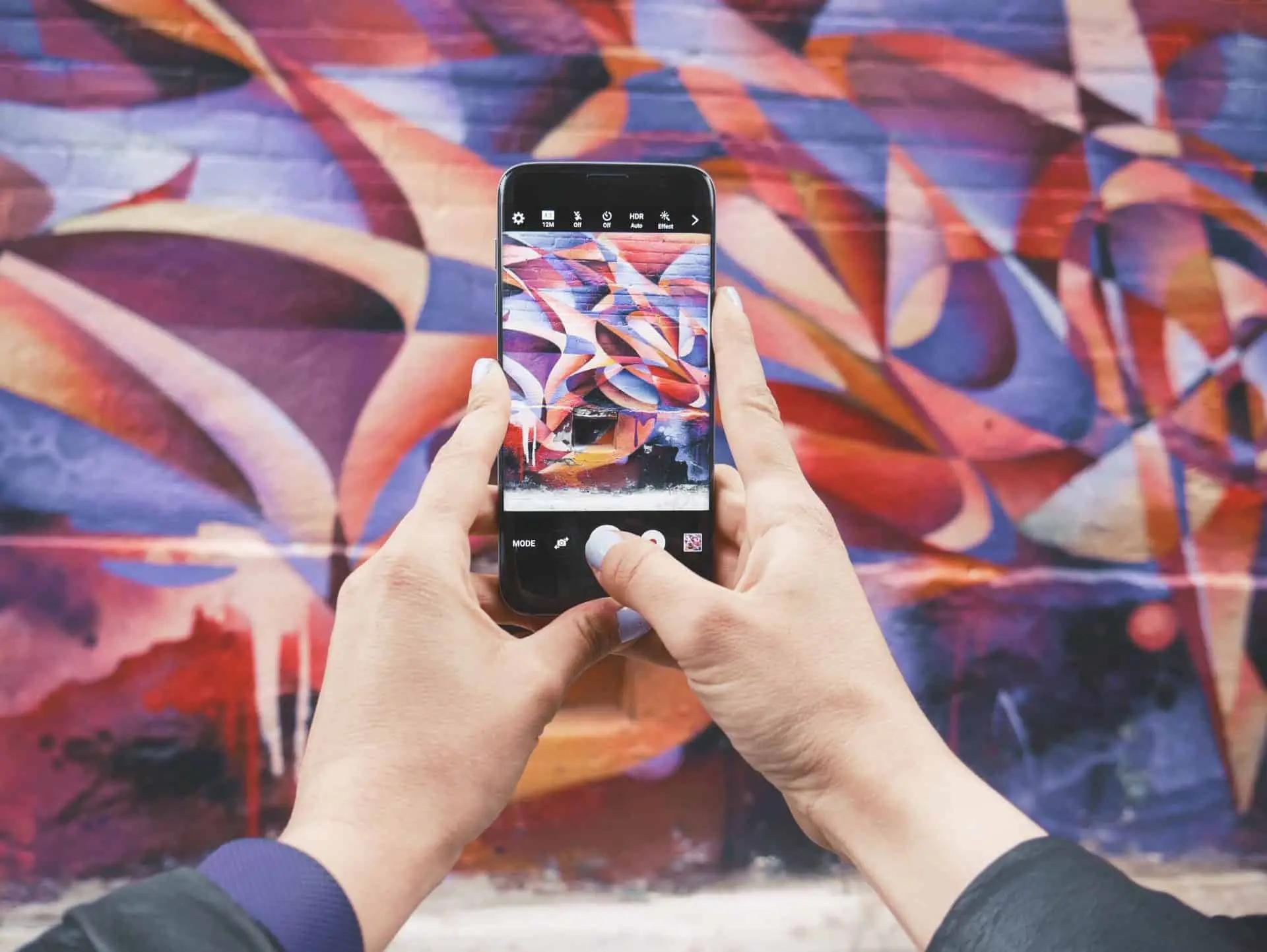 Hands holding a phone taking a photo of a colorful abstract mural in camera app view