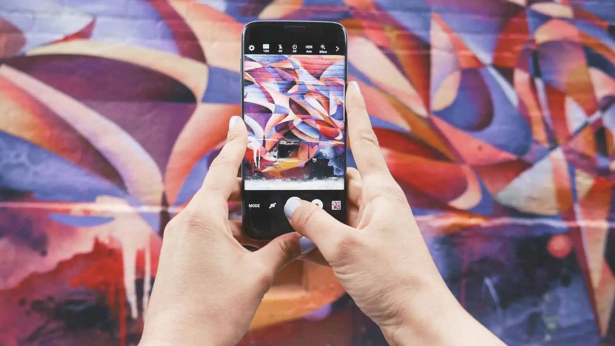 Hands holding a phone taking a photo of a colorful abstract mural in camera app view
