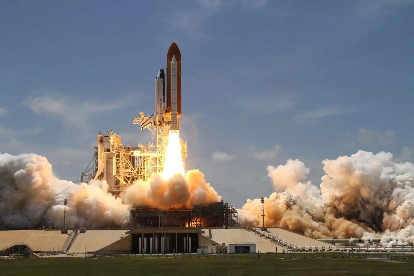 A space shuttle launching from a pad, engulfed in flames and billowing smoke